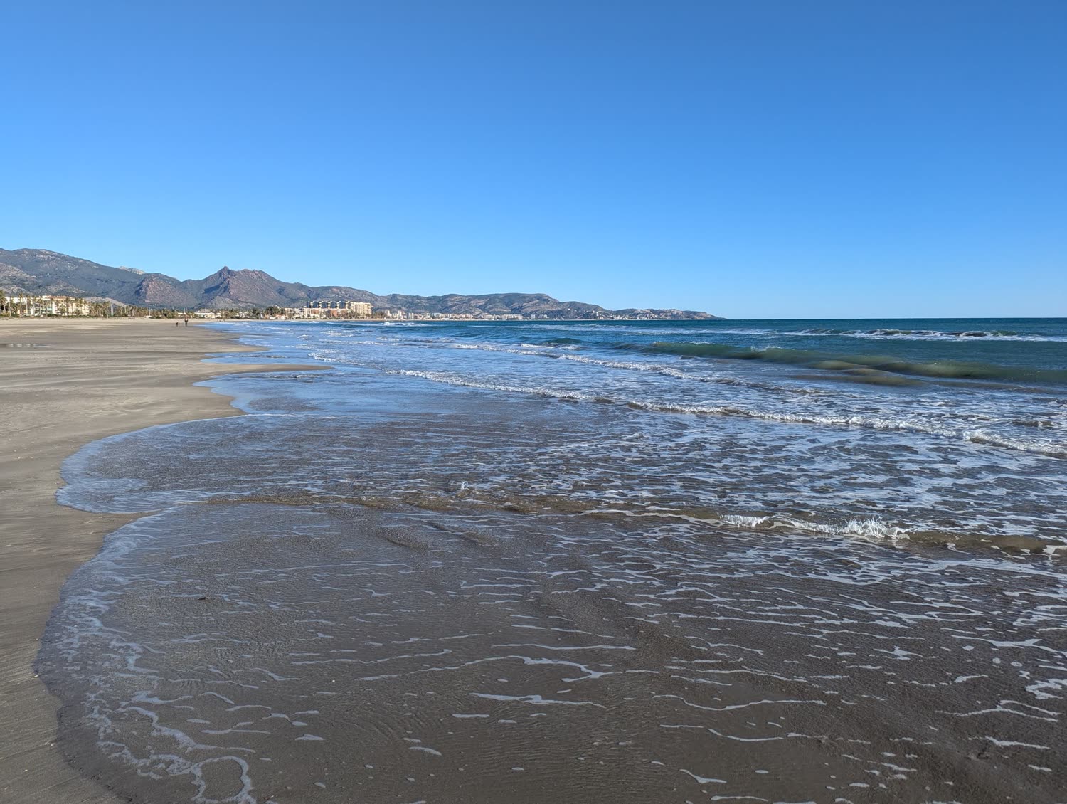 La playa en invierno, con las montañas y la ciudad al fondo.