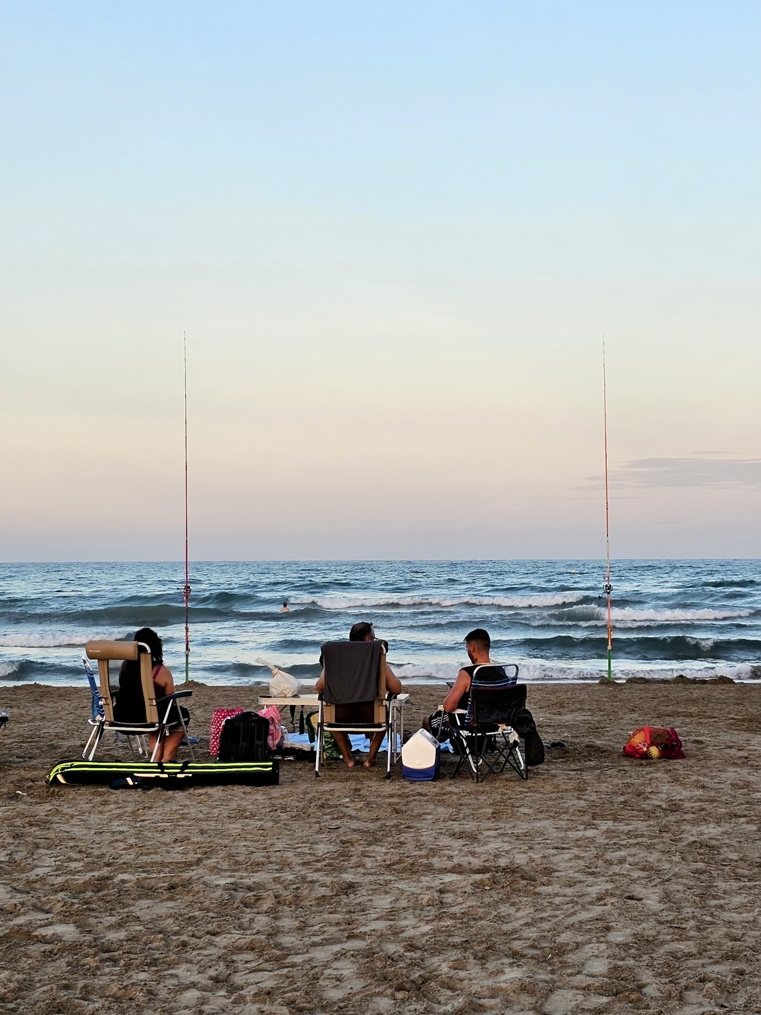 Tres pescadores con sus cañas en la playa al anochecer.