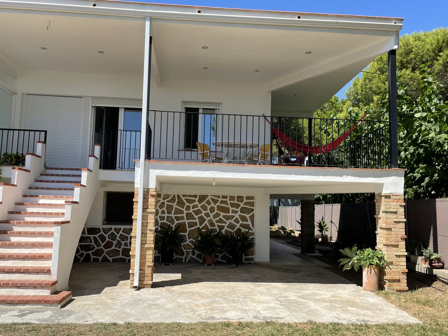 La casa entera desde el jardín, con la escalera de ladrillo y la terraza.